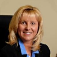 Headshot of Mary Pat Julias wearing black blazer and blue shirt with beige background