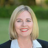 Headshot o Isabel Pease wearing black blazer, striped shirt with green blurred background