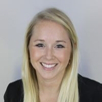 Headshot of Kara Barber wearing black blazer and orange shirt with gray background