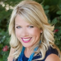 Headshot of Amy Glaser with blue shirt and blue necklace with bushes in the background