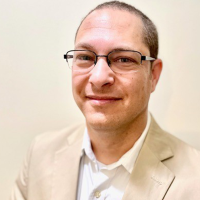 Headshot of Haim wearing beige blazer and white shirt with white background