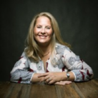 Headshot of Kristen Benjamin wearing multicolored shirt with black background