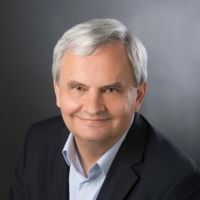 Headshot of Greg Gutkowski wearing black blazer and blue collared shirt with gray background