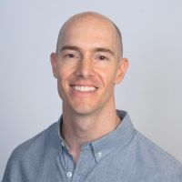 Headshot of Jeff R wearing a blue collared shirt with a light blue background