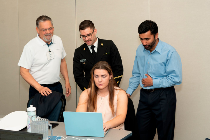 3 males and one female gathered around a laptop with a blue cover