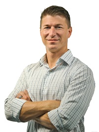 A headshot of Steve Elder wearing a plaid shirt with his arms crossed with a white background.
