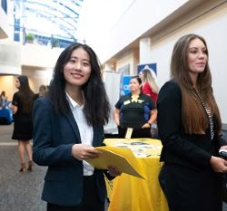 student smiling with a folder in her hand with students in the background