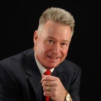 Headshot of Leonard Fritz with a suit, red tie and watch with a black background