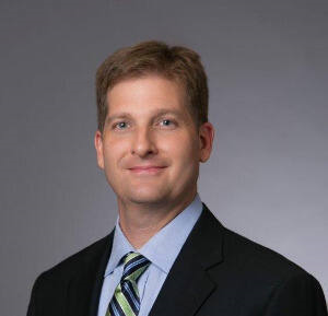 Headshot of William J Montford wearing black suit with green and blue striped tie