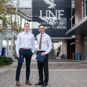Two students dressed in suits in front of UNF Banner