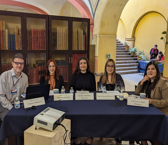 Panel of five individuals sitting at table, in front of bookshelf