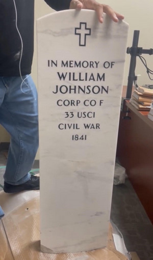 Man holding headstone that says "In Memory of WIlliam Johnson Corp CO F 33 USCI Civil War 1841