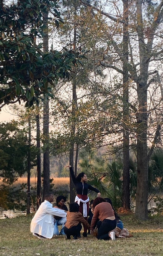 Six students crouching in a huddle with one in the middle standing, in the forest.