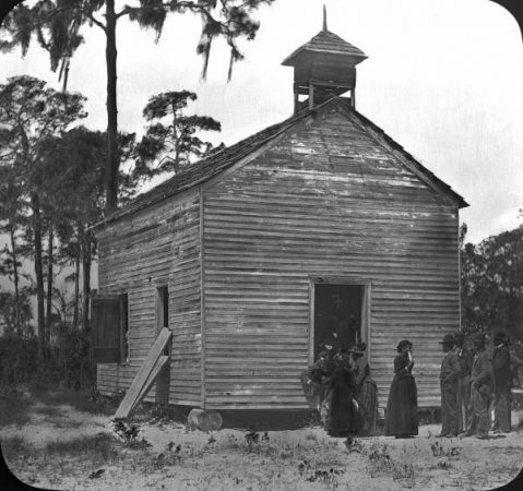 black and white old house with people in old fashioned clothes standing in front