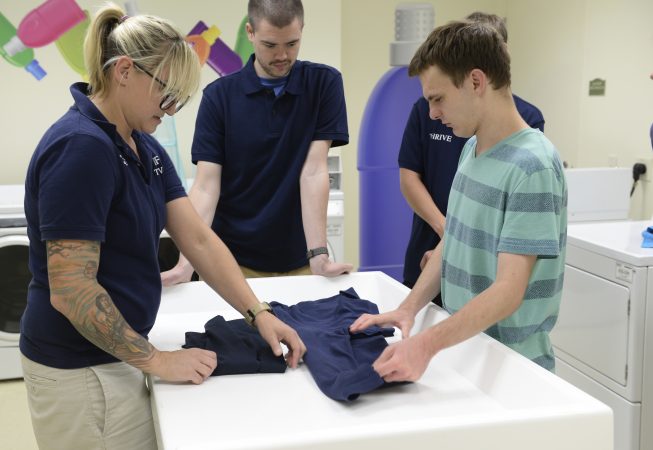 Staff member showing student how to fold clothing