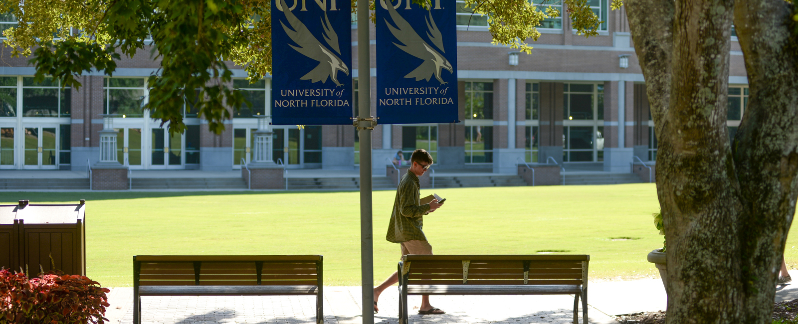 Student walking through UNF's campus by the green lawn with UNF signs on a lightpole