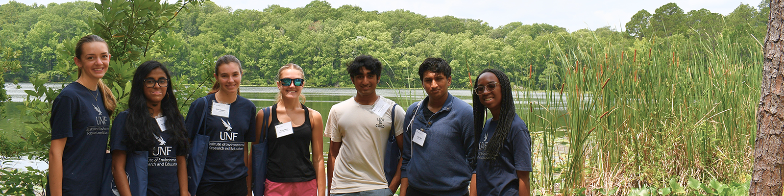 Seven individuals standing in front of a lake posing for a photo.