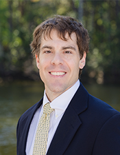 Headshot of Dr. Raphael Crowley standing outside with trees in the background.