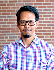 Headshot of Florentino De la Cruz standing in front of a brick wall. 