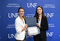 Dr. Largo-Wight presenting student of year award to Klesia in front of UNF logo background.