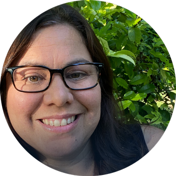 Headshot photo of Monica Magee with green foliage behind.