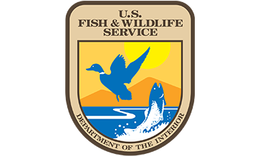logo of U.S. Fish and Wildlife Service featuring a duck flying above water and a fish coming jumping out of the water.