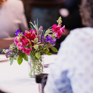 Bright flower arrangement in a glass jar on a round table.