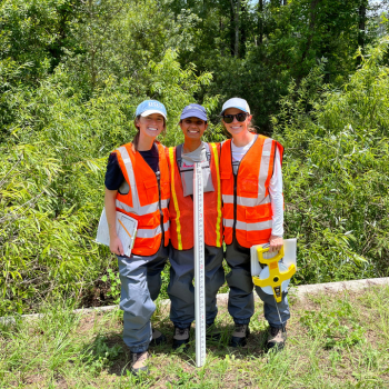 Three field researchers in safety vests posing with equipment