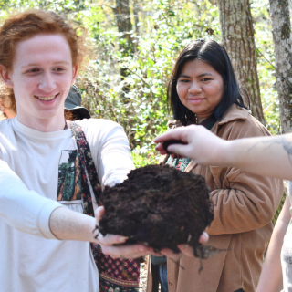 Individuals in a forest with one holding a pile of dirt.