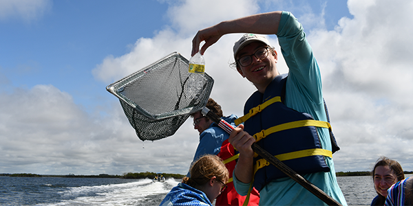 Individual in a boat holding up a net while collecting trash.
