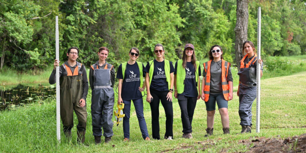 Field team posing with equipment beside pond edge