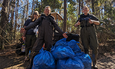 Three students standing behind blue bags of trash collected.