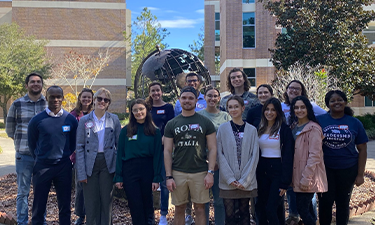 Group of fifteen students posing for a group photo outdoors.