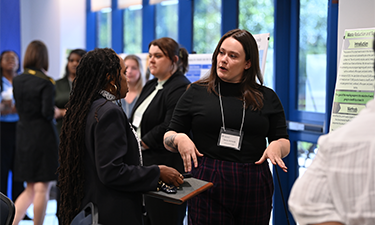 Dr. Karen Patterson having a conversation with Devon, an ELP student representative, discussing her project with her poster and other attendees in the background.