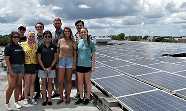 Group of eight individuals posing for a photo next to solar panels.