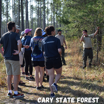 Group of students standing in preserve while on an educational hike with the wording Cary State Forest written on the bottom of the photo.