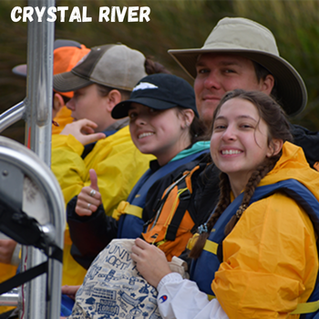 Three individuals smiling while riding in a boat wearing life jackets with the location of Crystal River written on the top left.