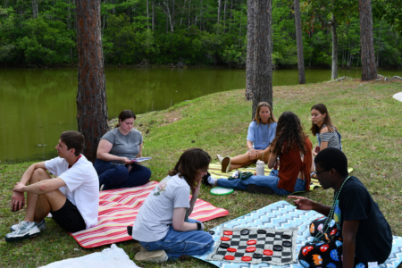 Students on a lawn by a lake relaxing and playing games