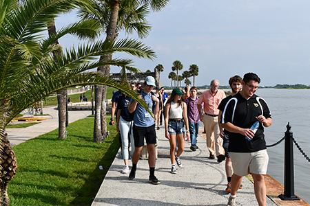 Students walking on path in-between waterway and greenery. 