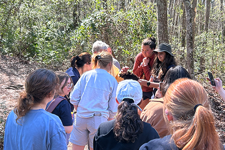 Group gathered in forest, some faces not clearly visible.