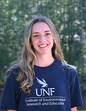 Headshot photo of student standing outdoors with nature background.