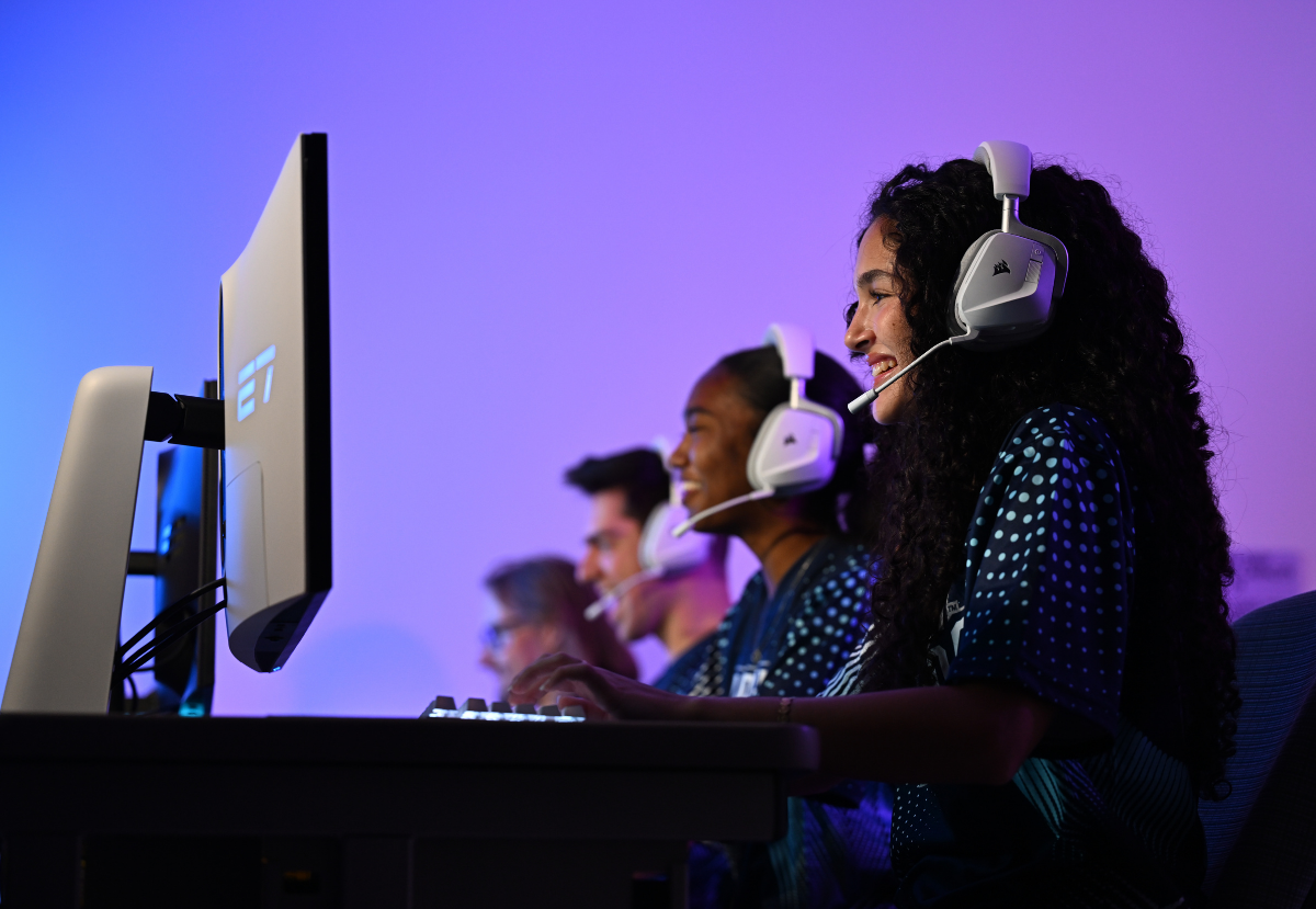4 smiling students playing video games at monitors