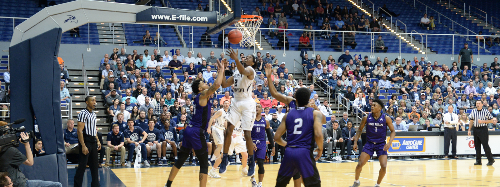 UNF's men basketball team at a game with a player tossing the ball into the hoop