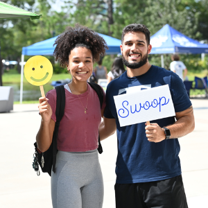 Two UNF students holding up a smiley face and a Swoop sign both smiling