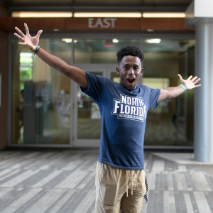 Male student with his hands extended in a UNF t-shirt