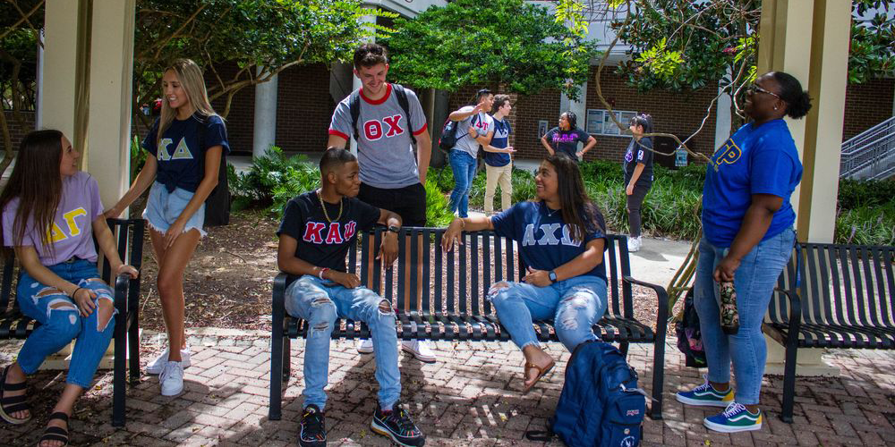members of the greek community sitting on benches and talking on campus