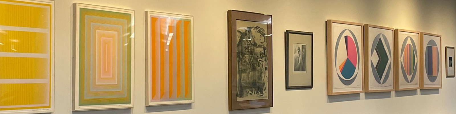 A collection of framed abstract artworks displayed on a gallery wall, featuring vibrant colors and geometric patterns.