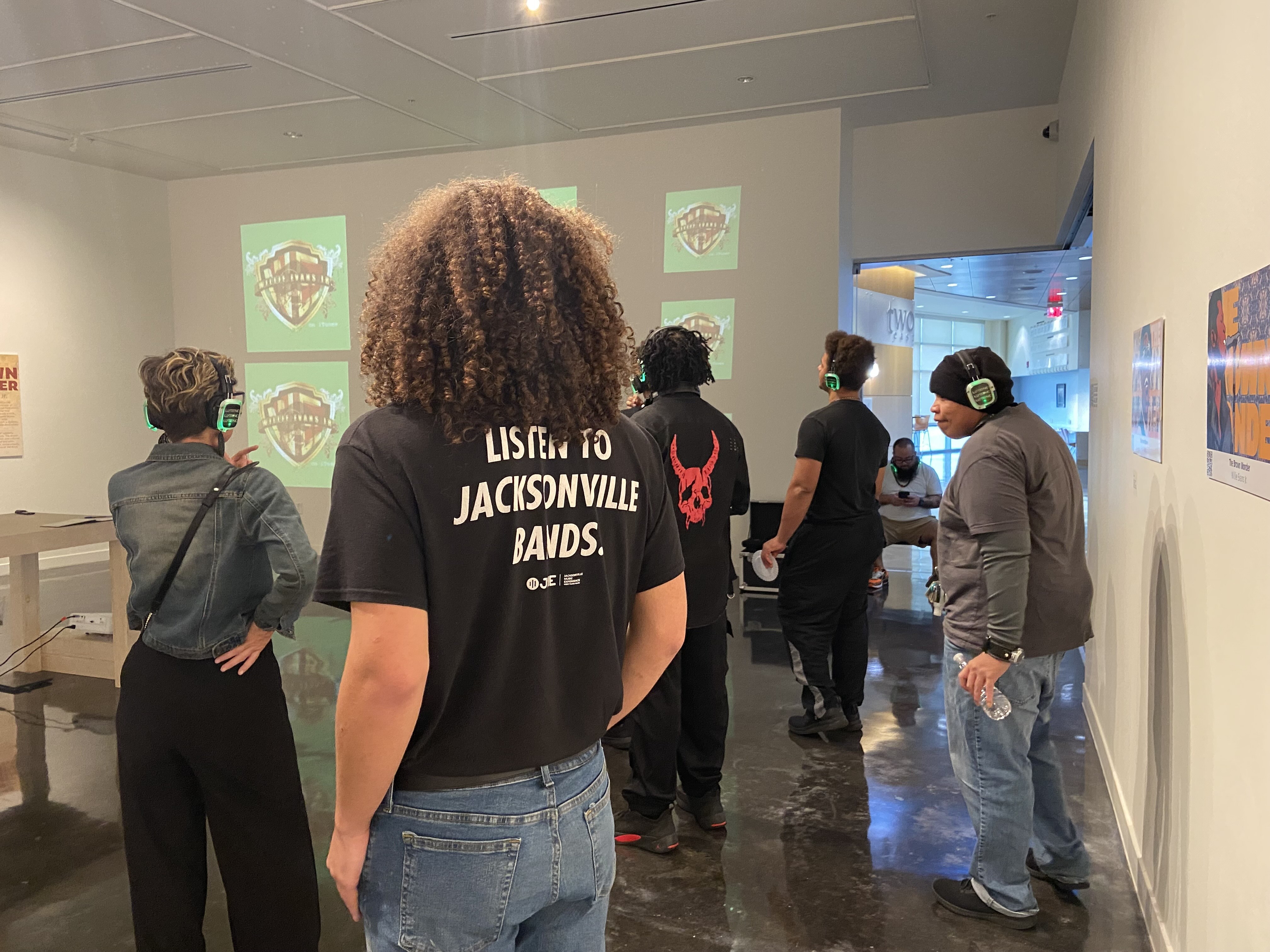 A group of people wearing headphones views a digital presentation on a screen in an art gallery.