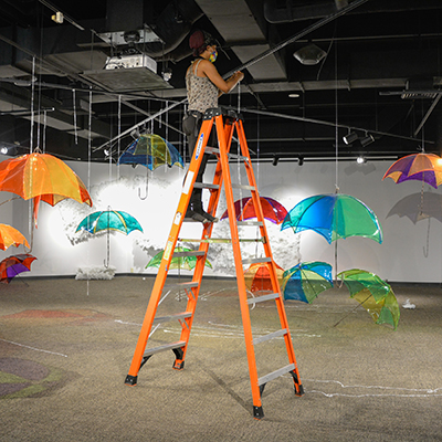 artist standing on a ladder hanging umbrella installation