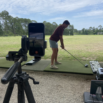 golf student on driving range with phone video recording
